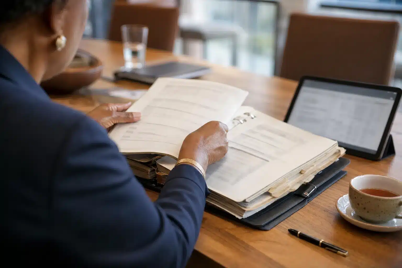 B-BBEE transformation lessons: a senior consultant turns pages of a worn ring binder beside a tablet in a boardroom